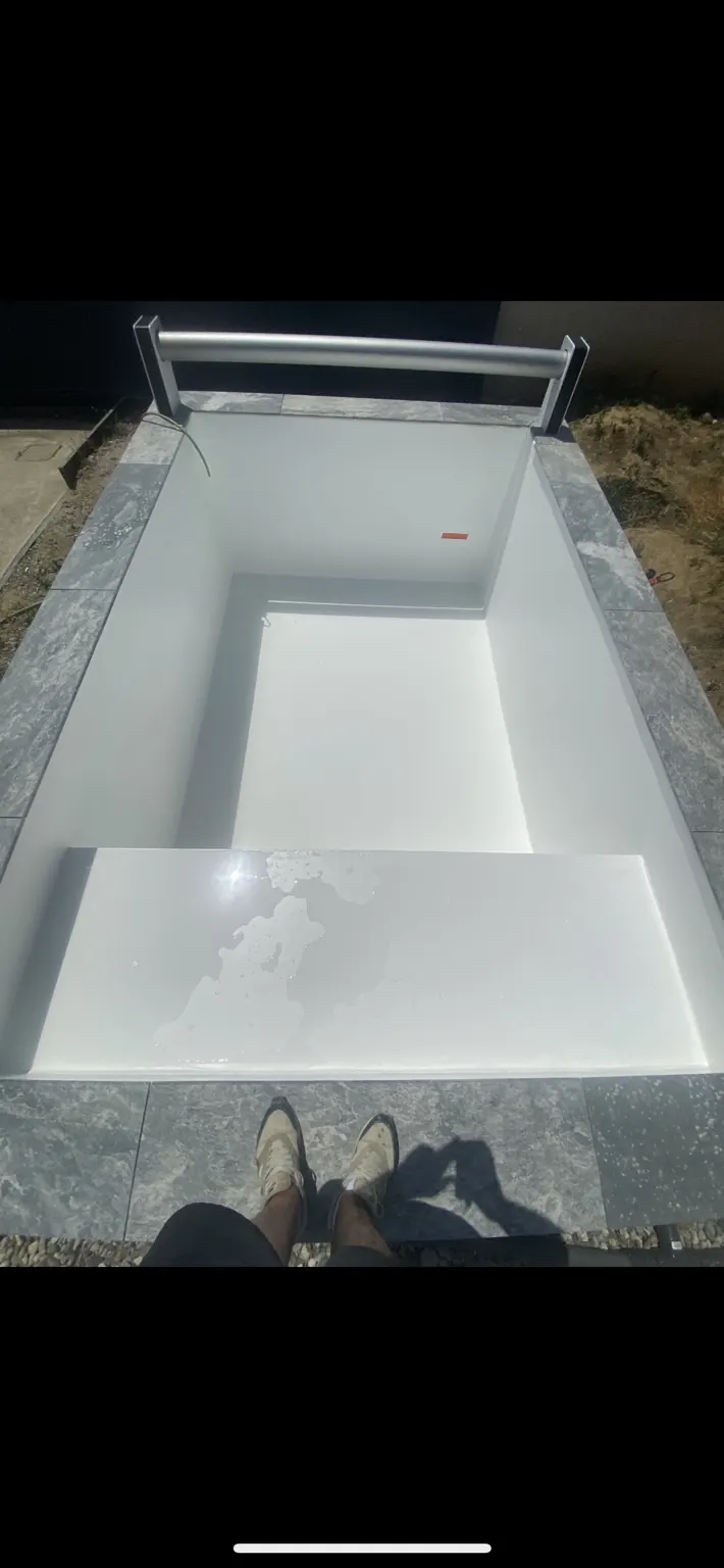 Bassin vide au revêtement clair, avec banquette et enrouleur en bout de piscine.
