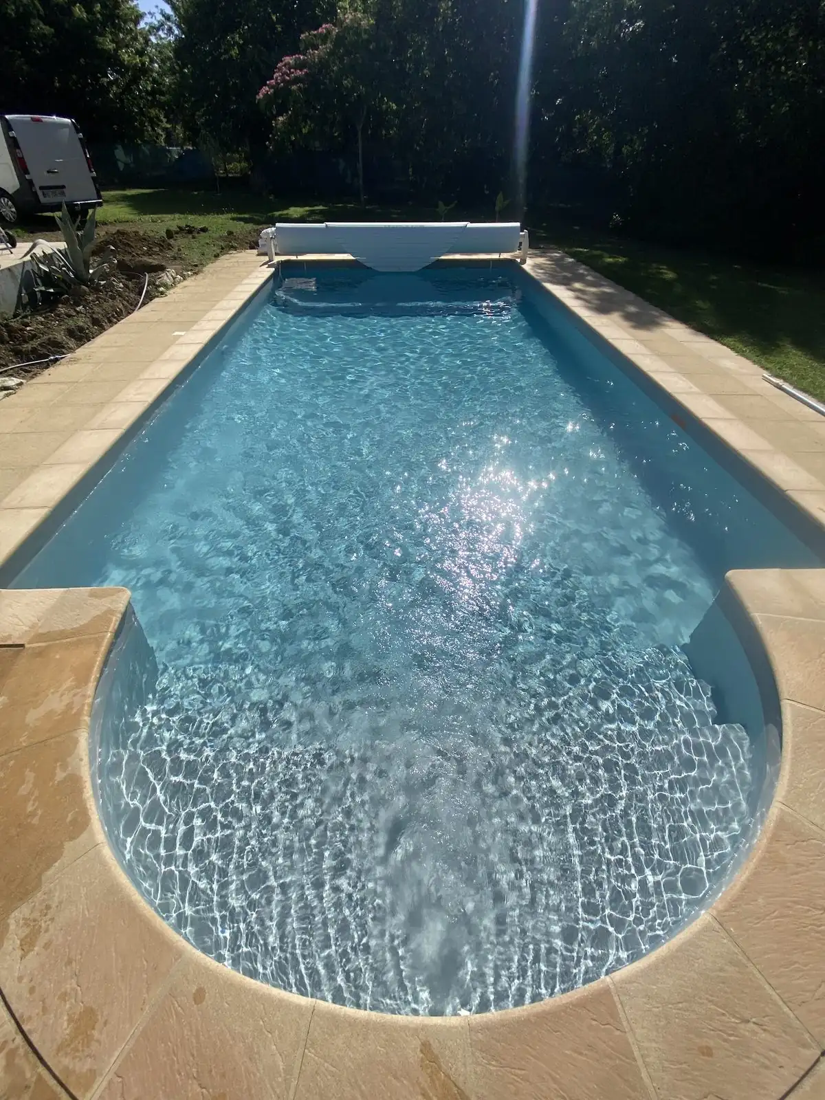 Piscine extérieure terminée avec escalier arrondi et volet roulant.