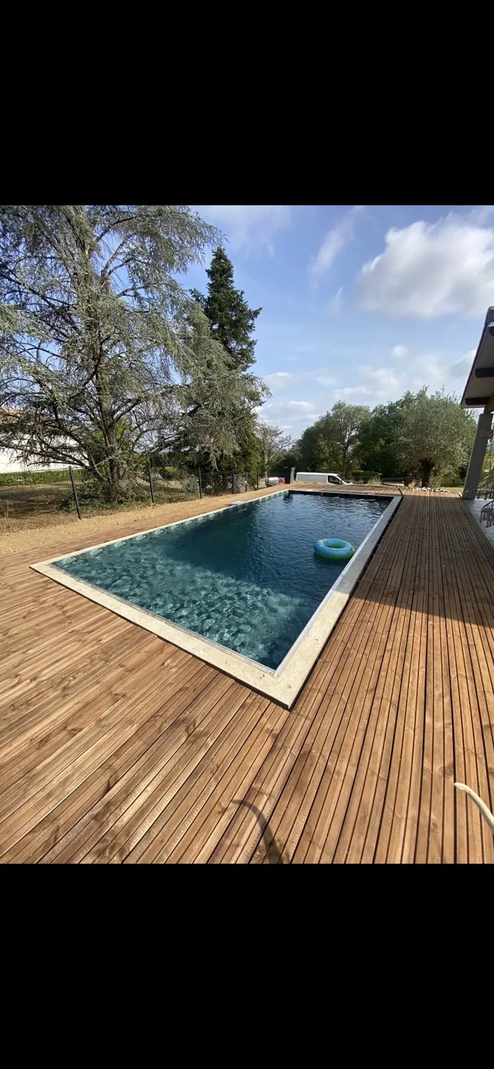 Vue de la piscine rectangulaire depuis la terrasse en bois.