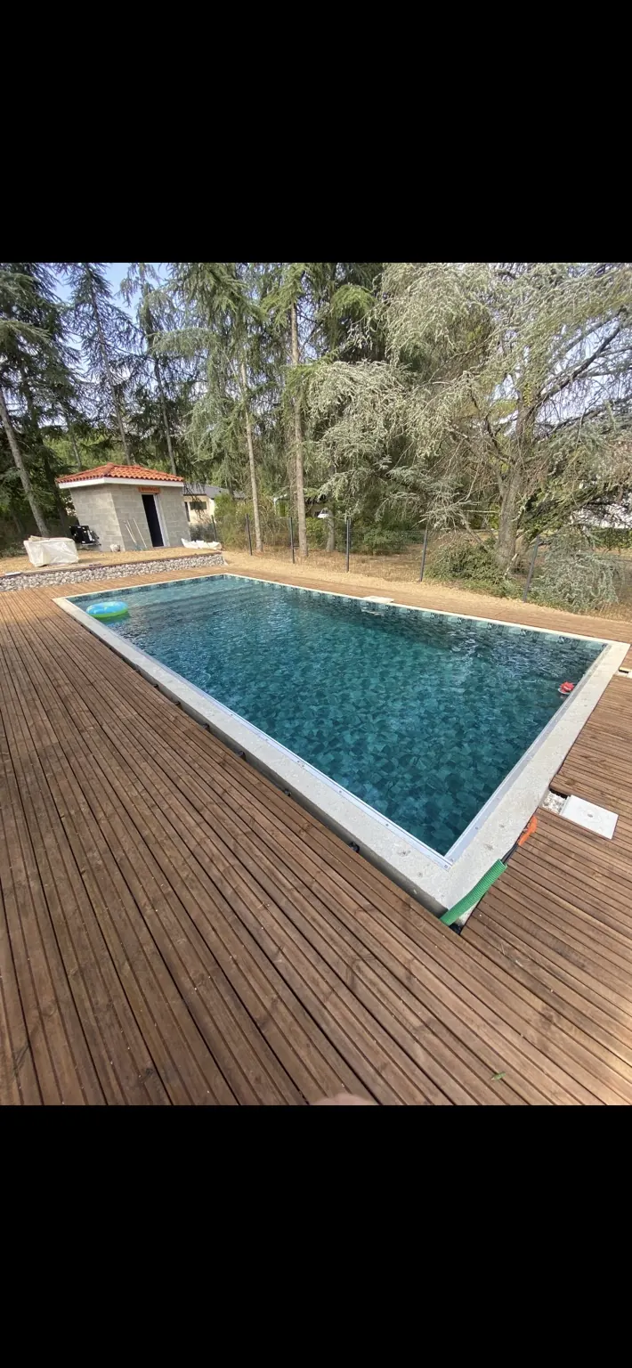 Piscine rectangulaire en eau avec terrasse en bois et arbres.