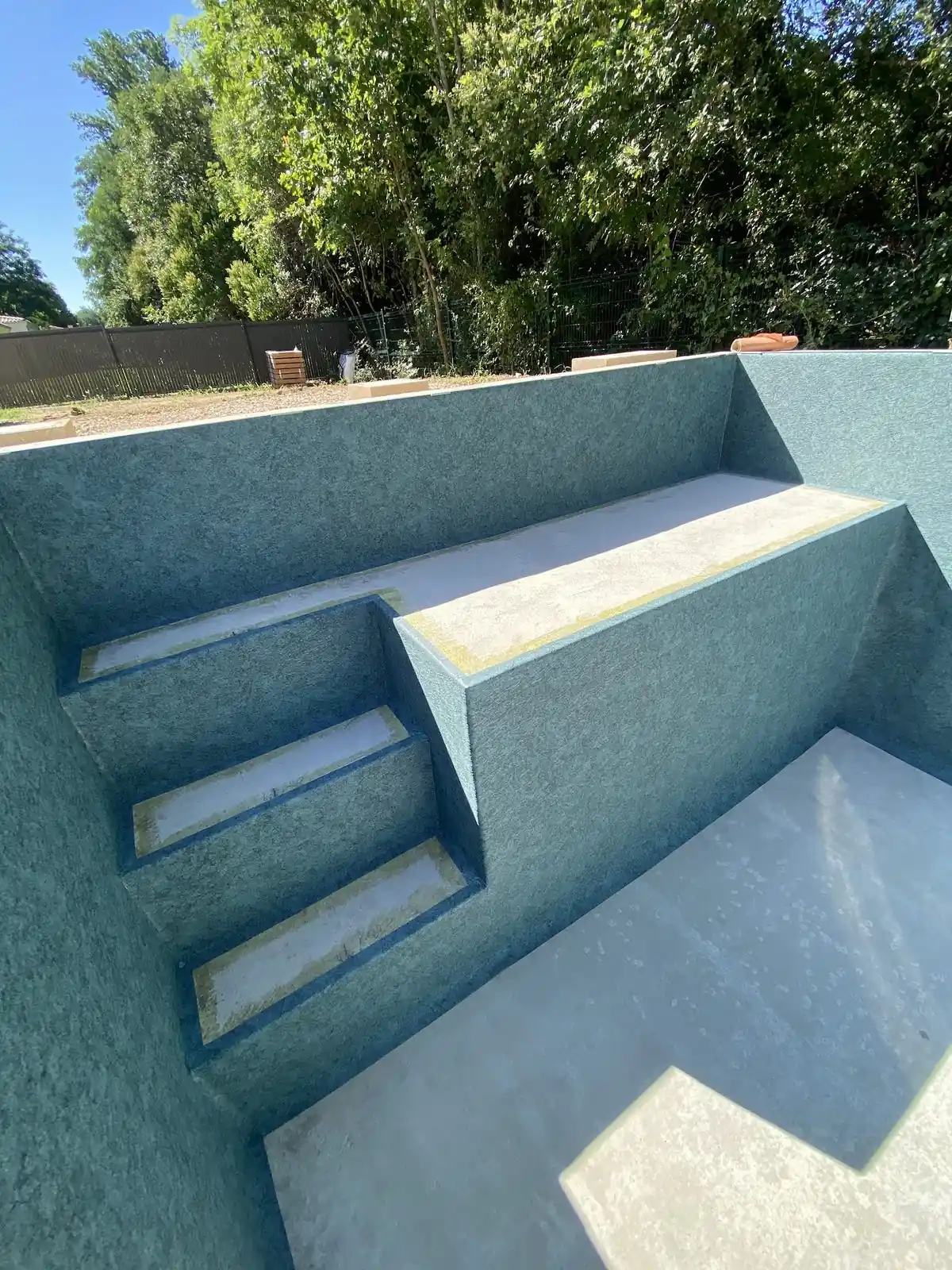 Bassin vide avec revêtement bleu et escalier intégré pendant une rénovation.